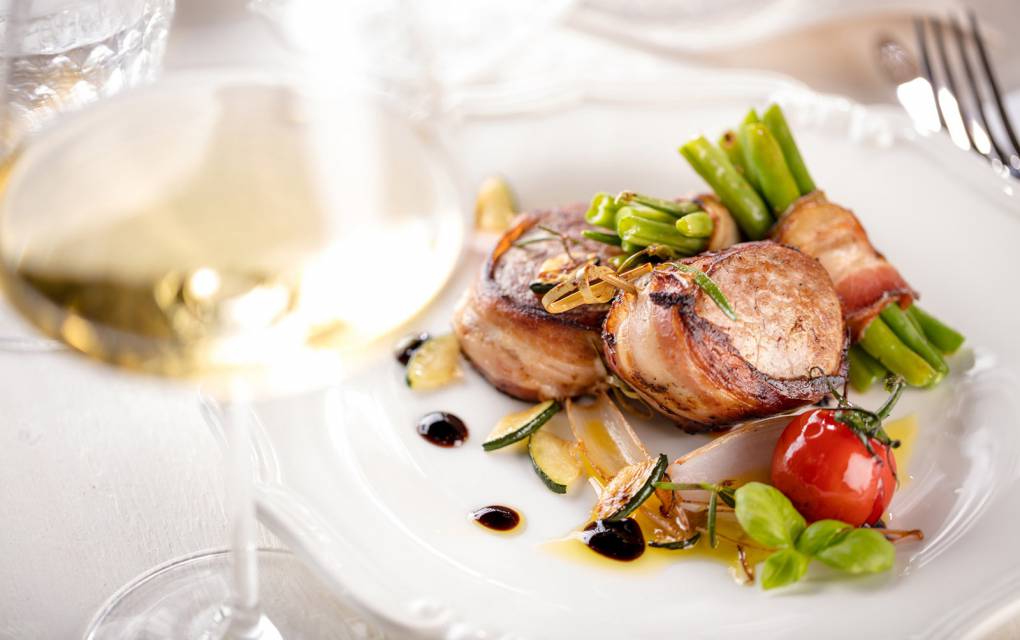 Schweinemedallions im Speck mit Bohnen und Weinglas angerichtet