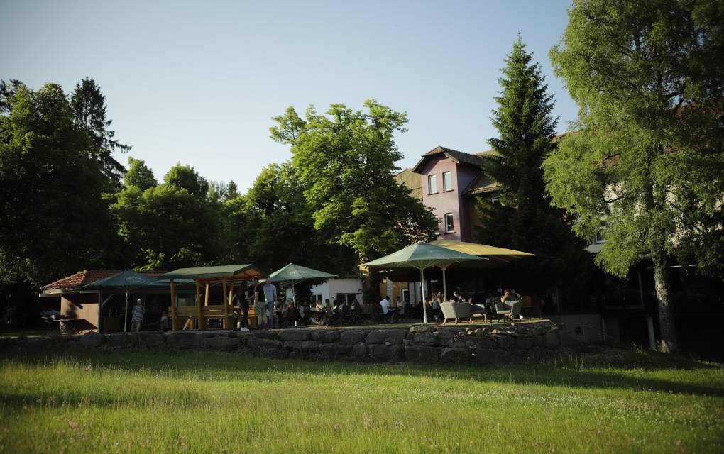 Außenterrasse mit Schirm und Tischen umgeben von Bäumen und Wiese