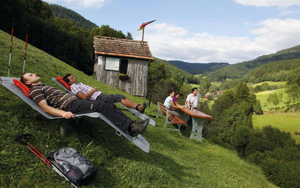 Wanderer machen eine Pause auf einer Liege am Berg mit Ausblick ins Tal