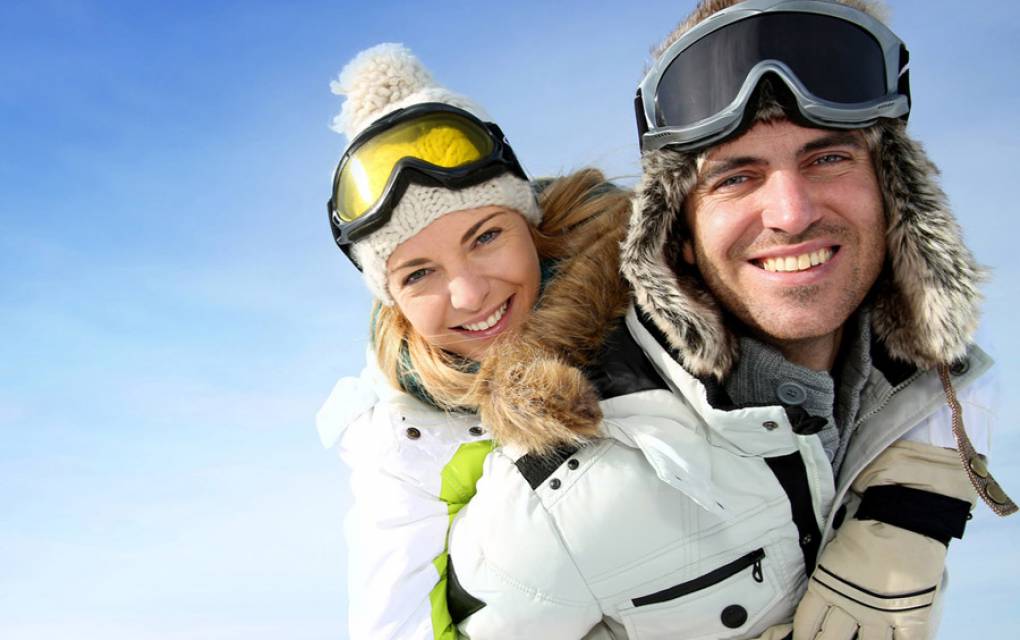 Paar in Skioutfits umarmen sich und schauen in die Kamera
