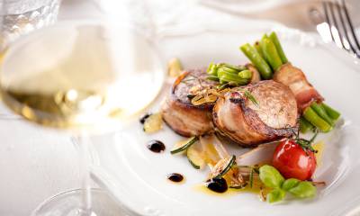 Schweinemedallions im Speck mit Bohnen und Weinglas angerichtet