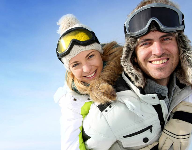 Paar in Skioutfits umarmen sich und schauen in die Kamera