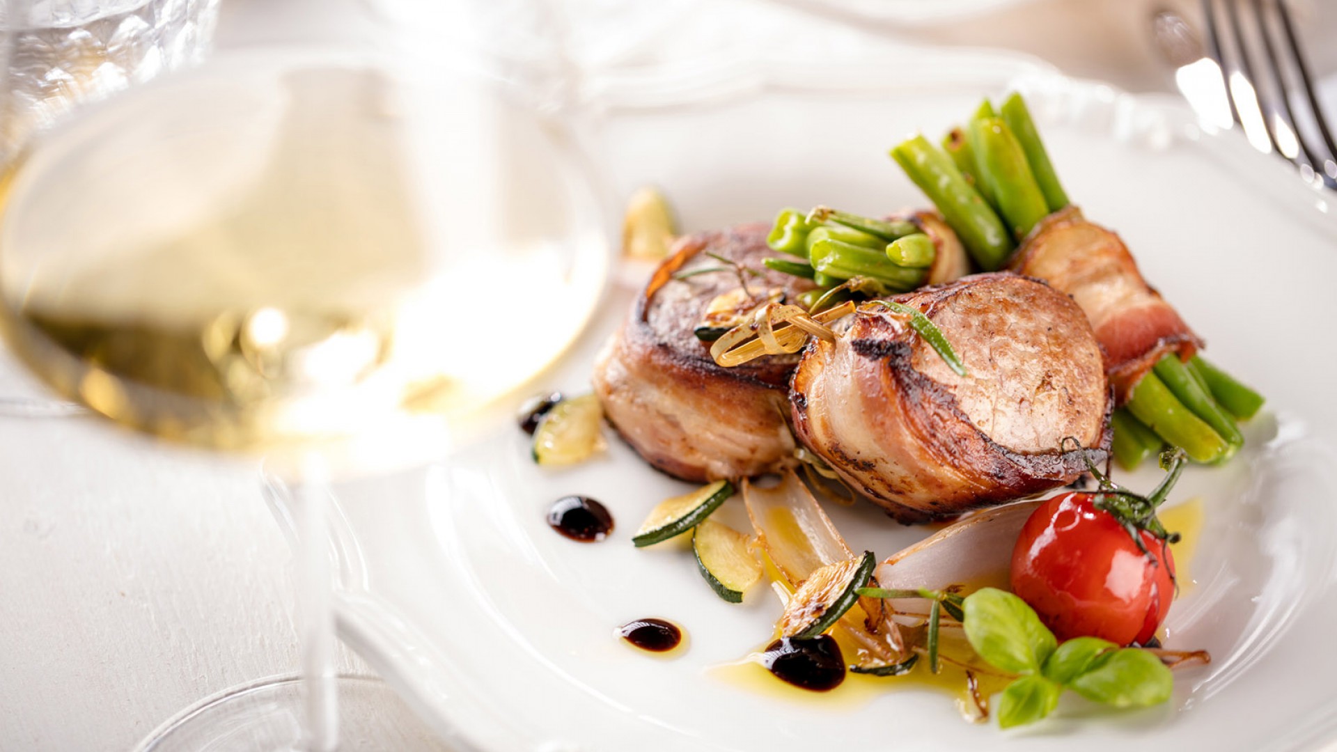 Schweinemedallions im Speck mit Bohnen und Weinglas angerichtet